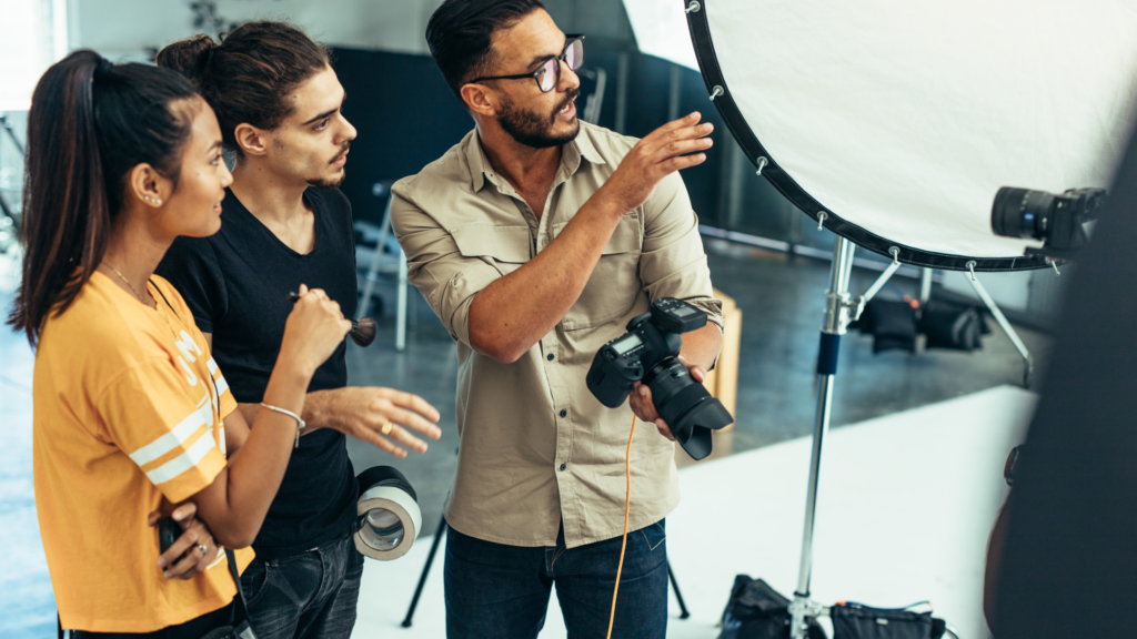 man holding a camera gives direction to to two people on set